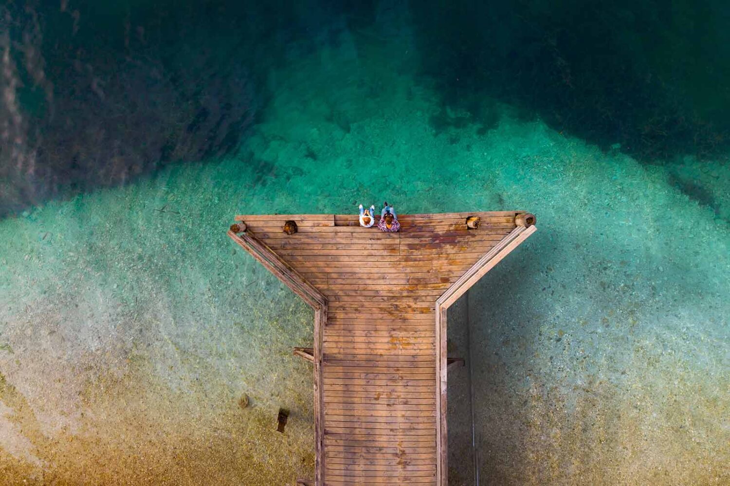 aerial view of people sitting on the end of a dock over the water